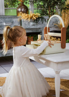 Young girl in a white dress interacting with a toy purse at a small table outdoors.