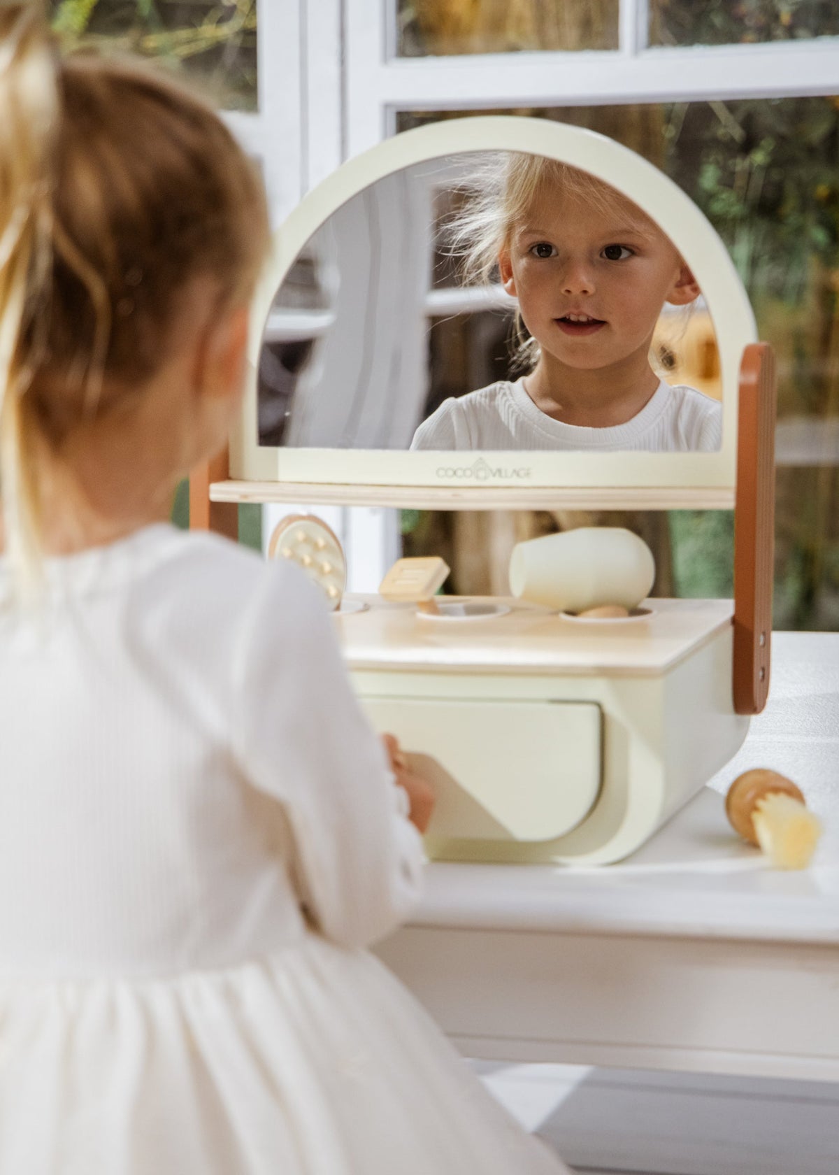 Child playing with a wooden toy vanity set in a bright room.