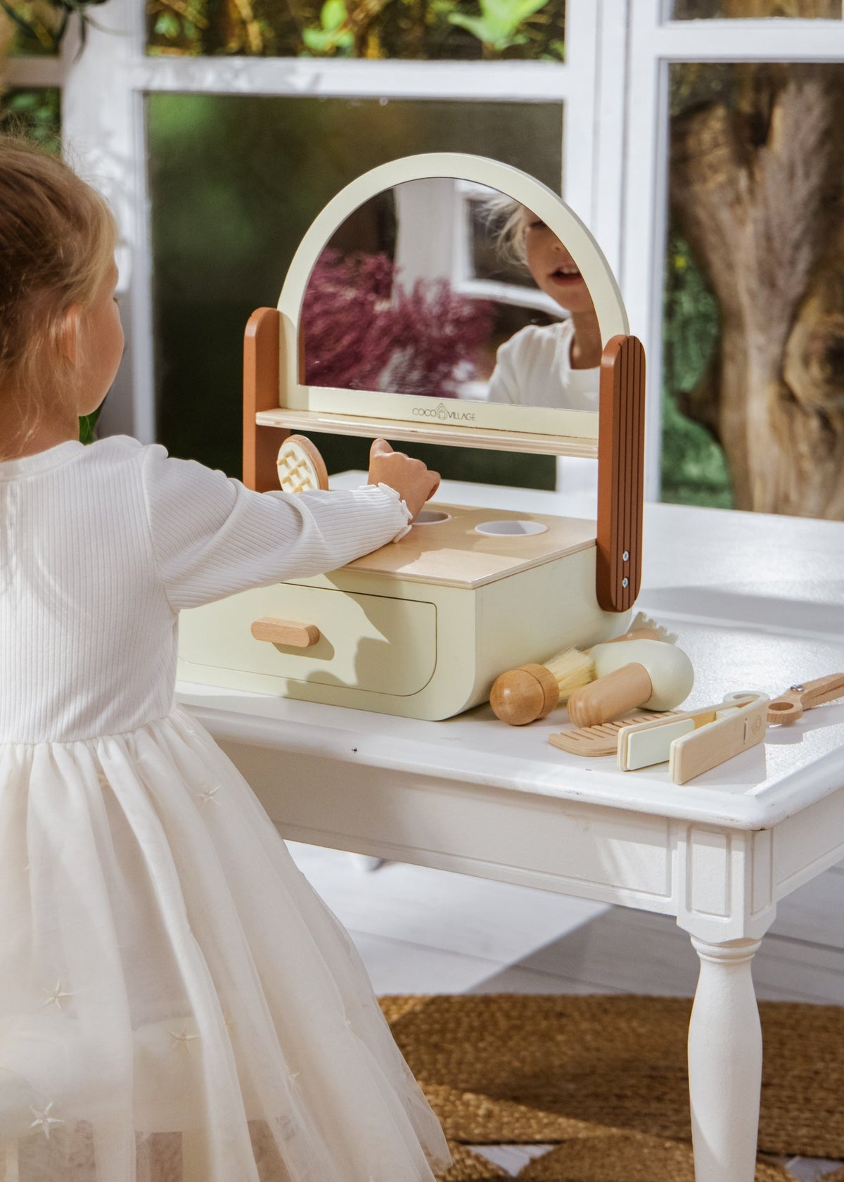Child playing with a wooden toy kitchen set on a table outdoors.