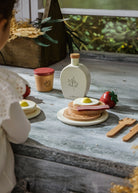 Children's play food set on a wooden table with a child partially visible.