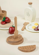 Wooden toy food set including a waffle, strawberries, and a plate with eggs and bacon on a light background.