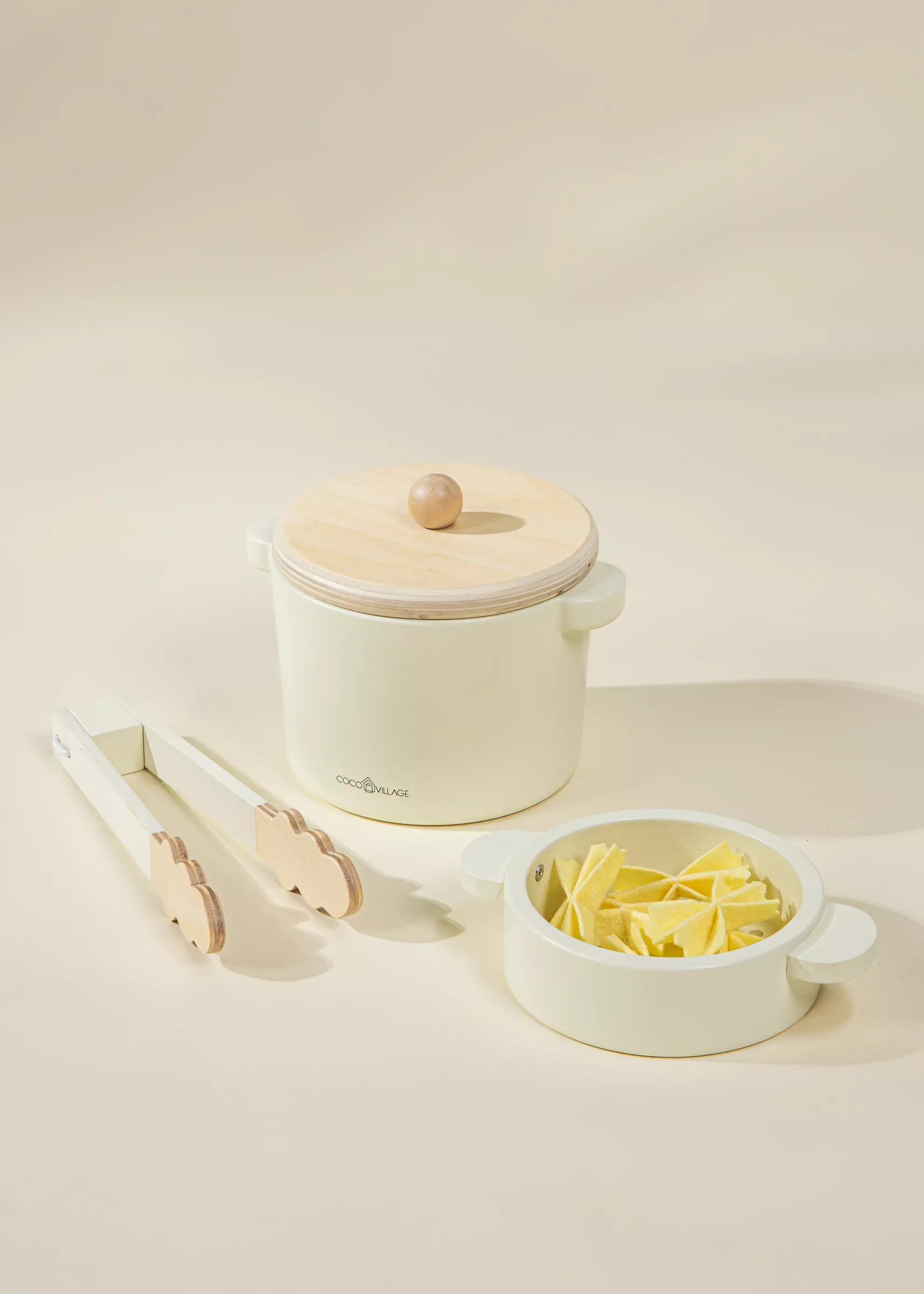 Small kitchen appliance with a lid, tongs, and a bowl of pasta on a light background