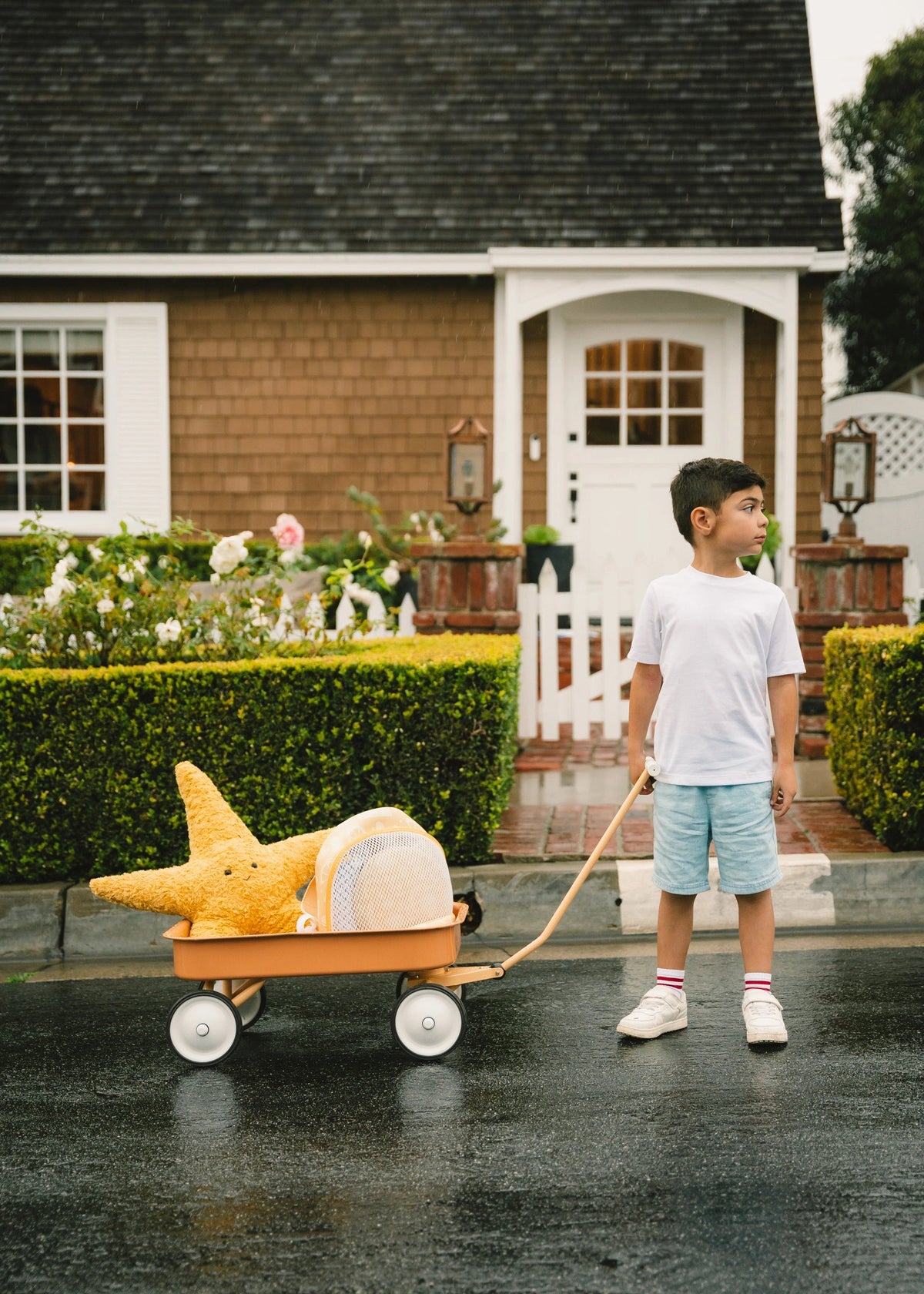Child pulling a cart with a shark toy in front of a house