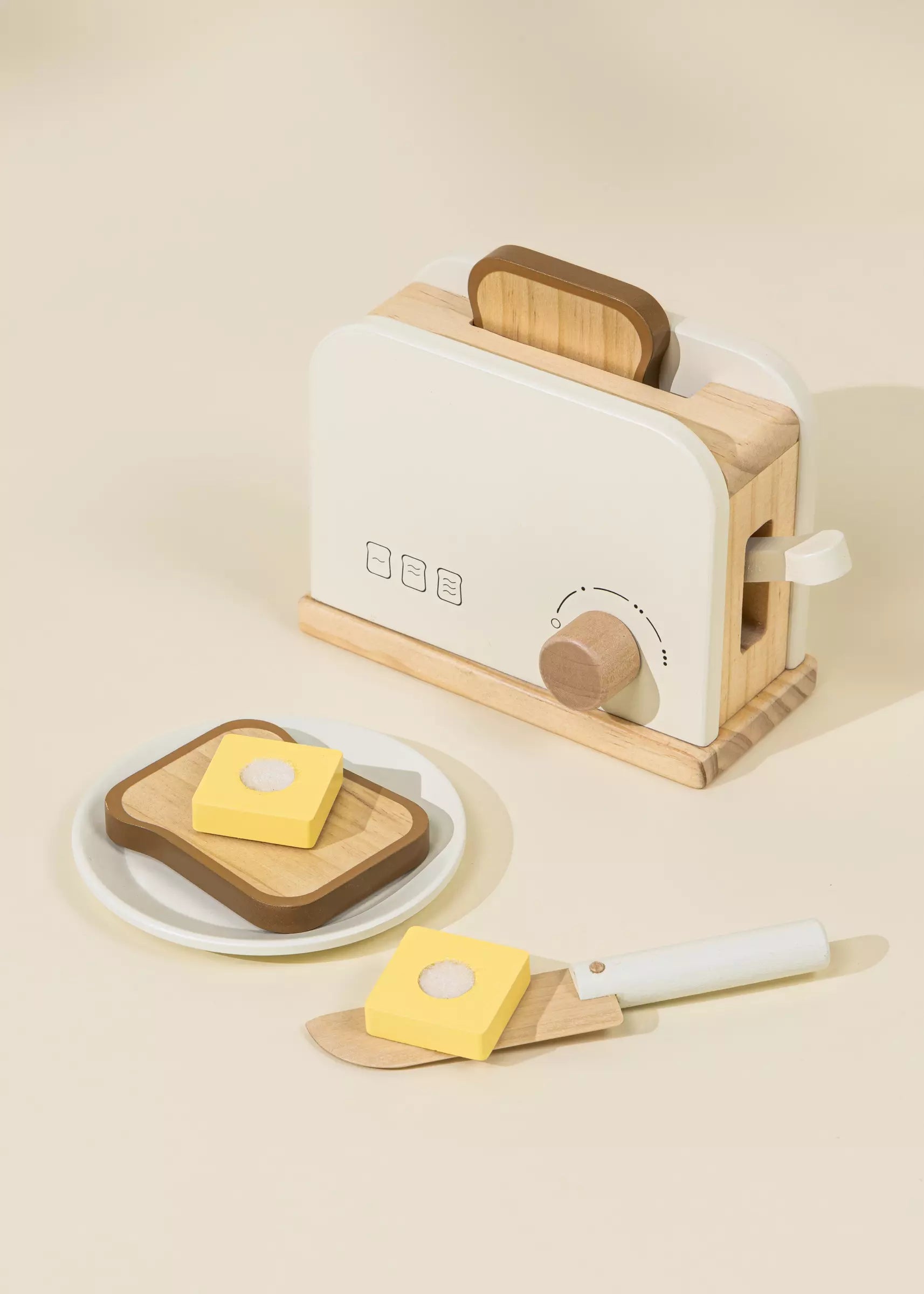 Wooden toy toaster with bread and butter on a beige background
