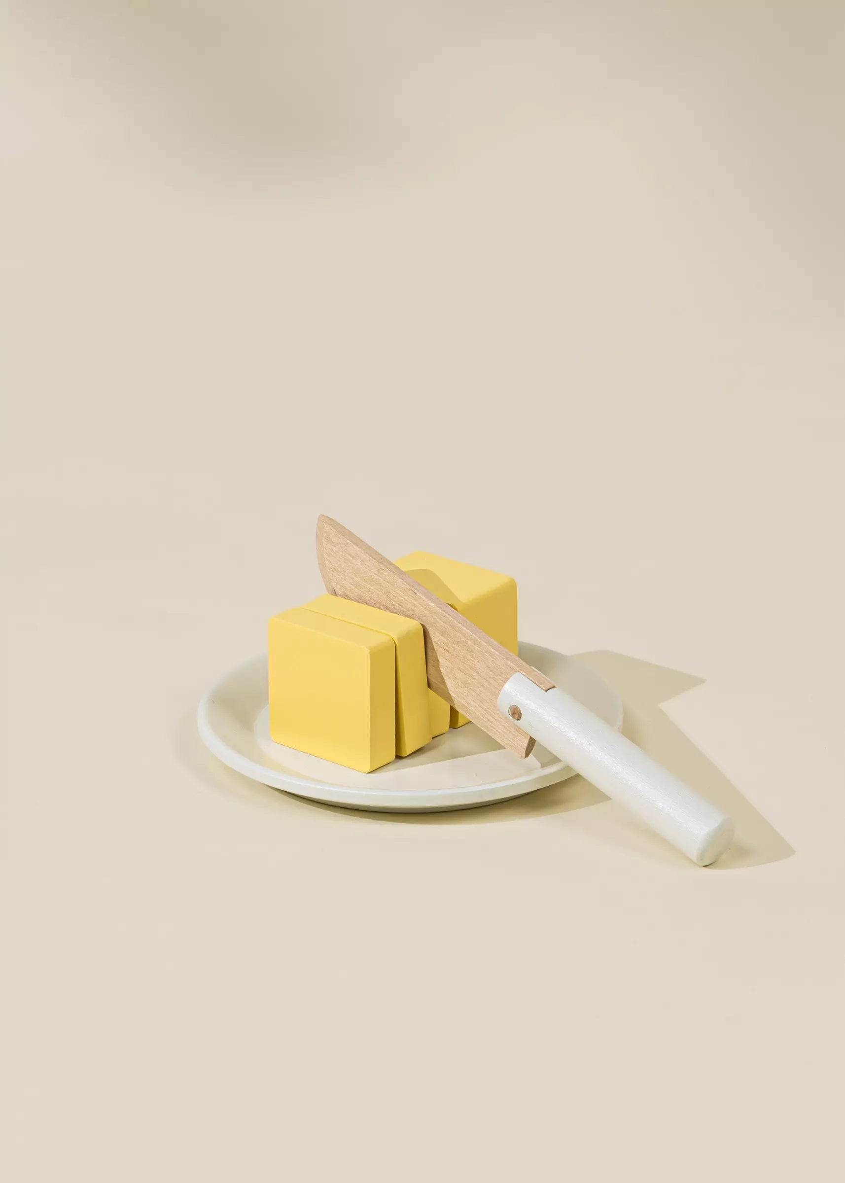 Three yellow soap bars on a white plate with a wooden knife on a beige background