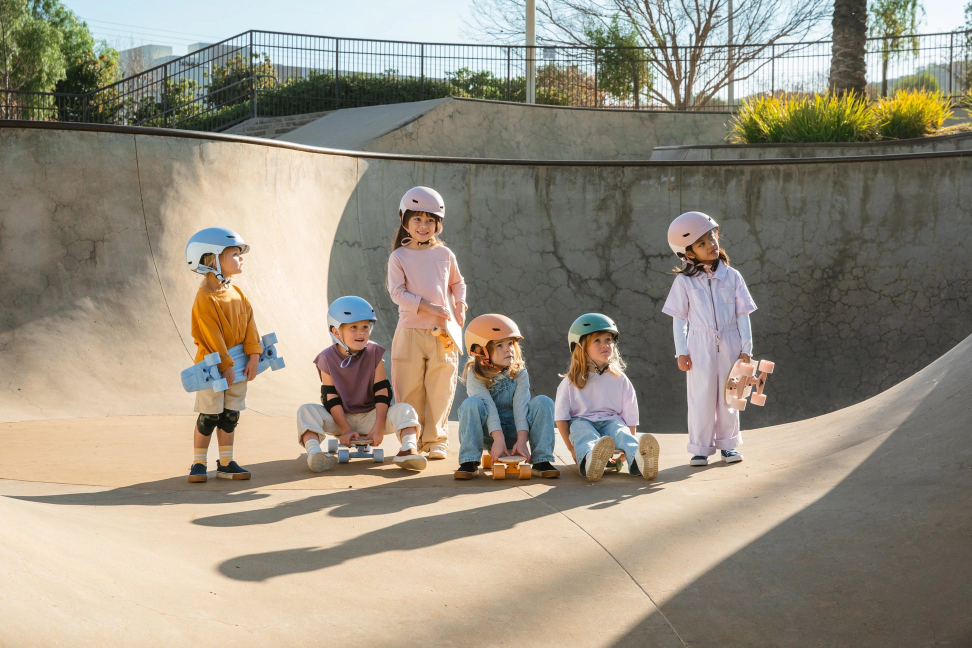 Children with skateboards and safety gear at a skate park.