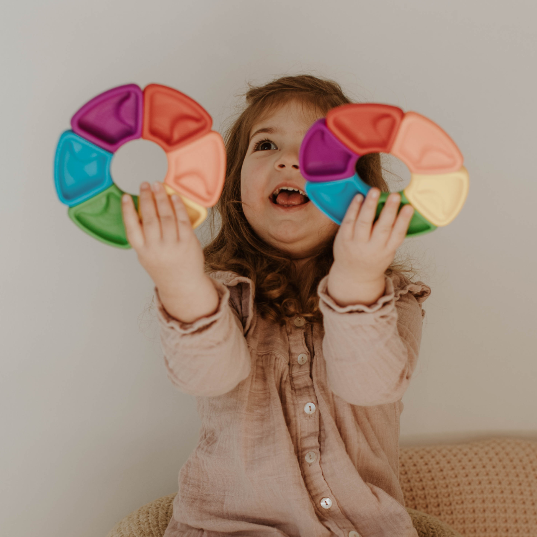 Child holding two colorful rainbow toys against a neutral background