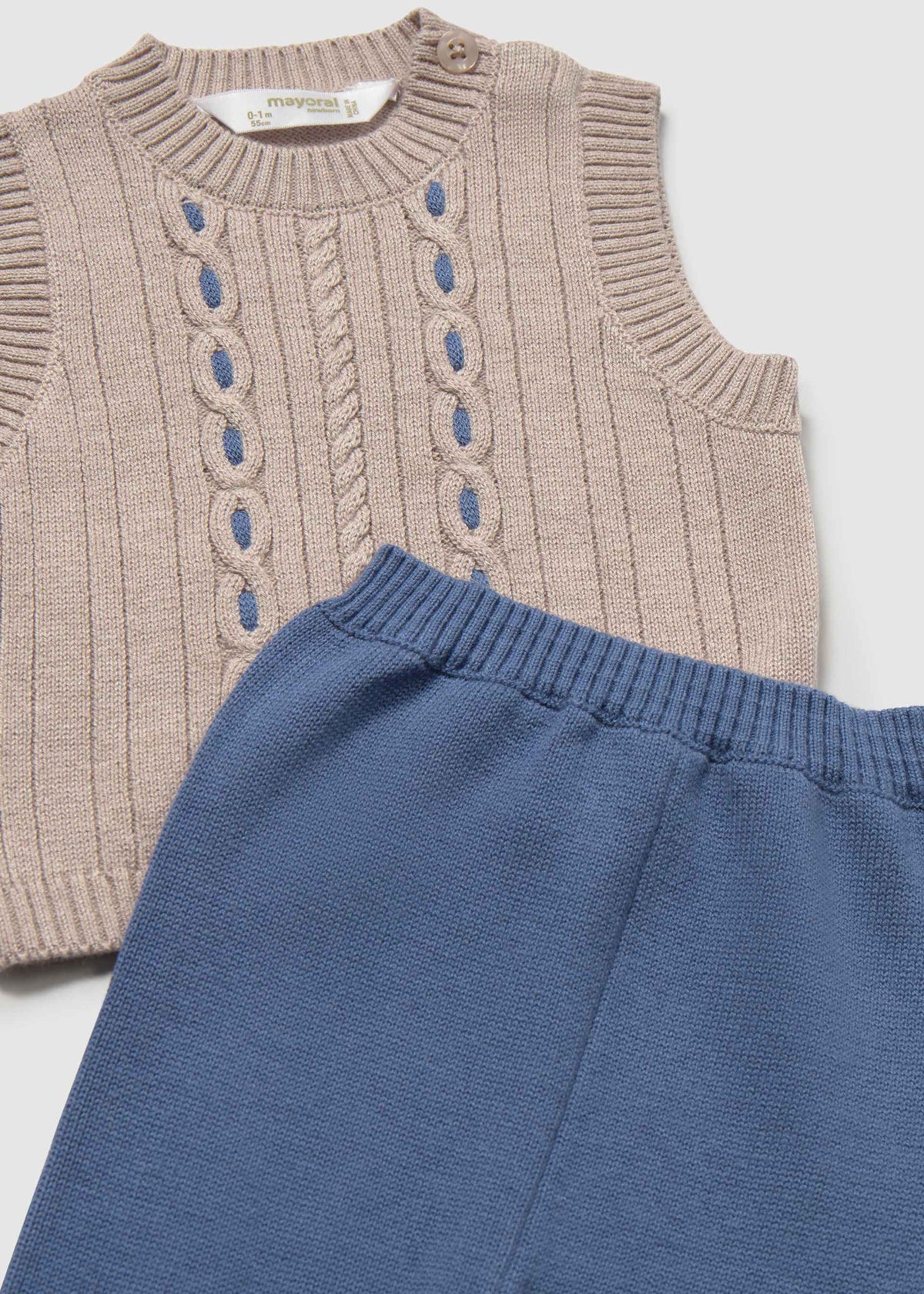 Knitted sleeveless top with cable pattern and blue pants on a light gray background