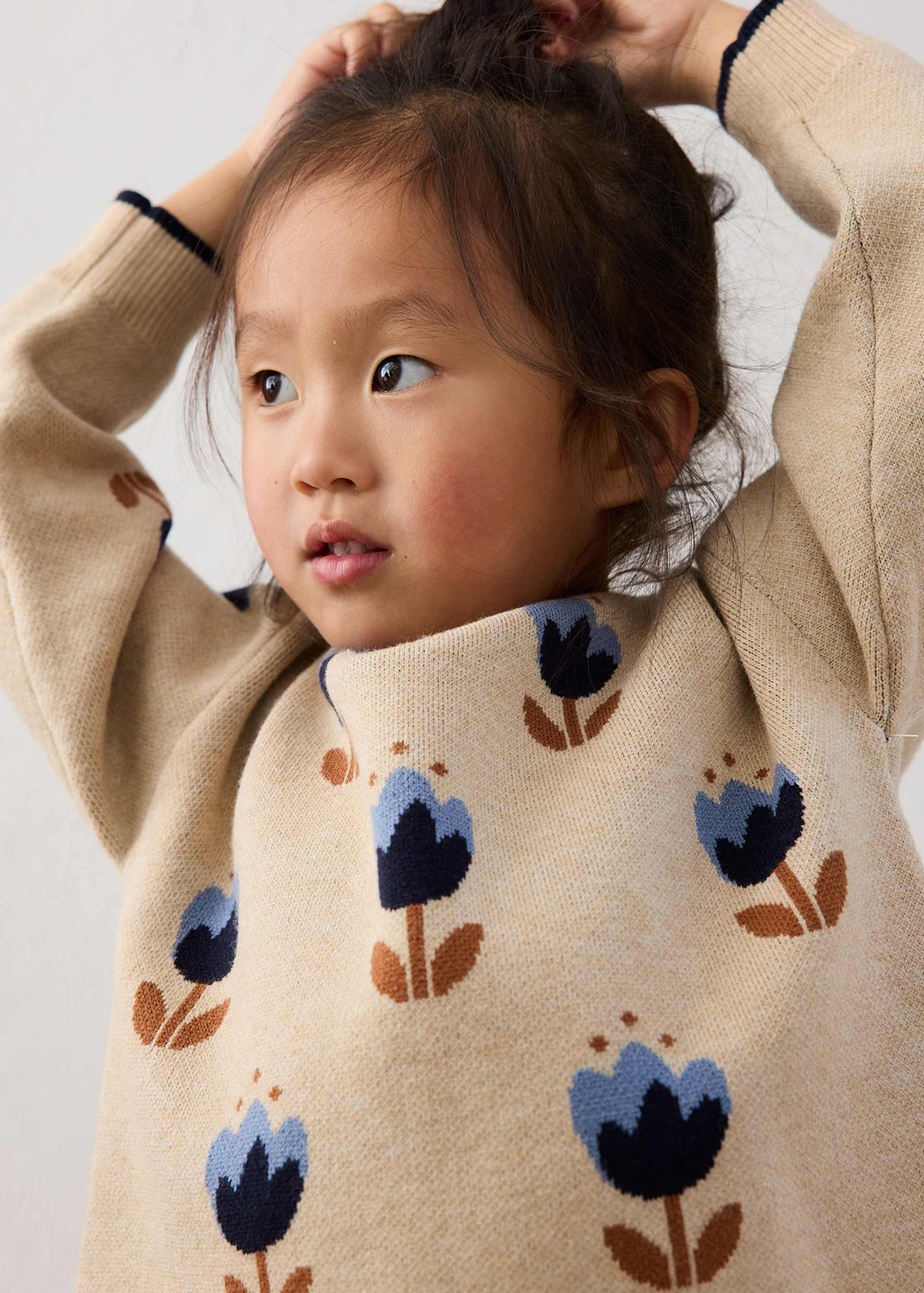 Child wearing a beige sweater with blue floral patterns on a plain background
