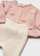 Pink knitted cardigan and beige pants on a white background