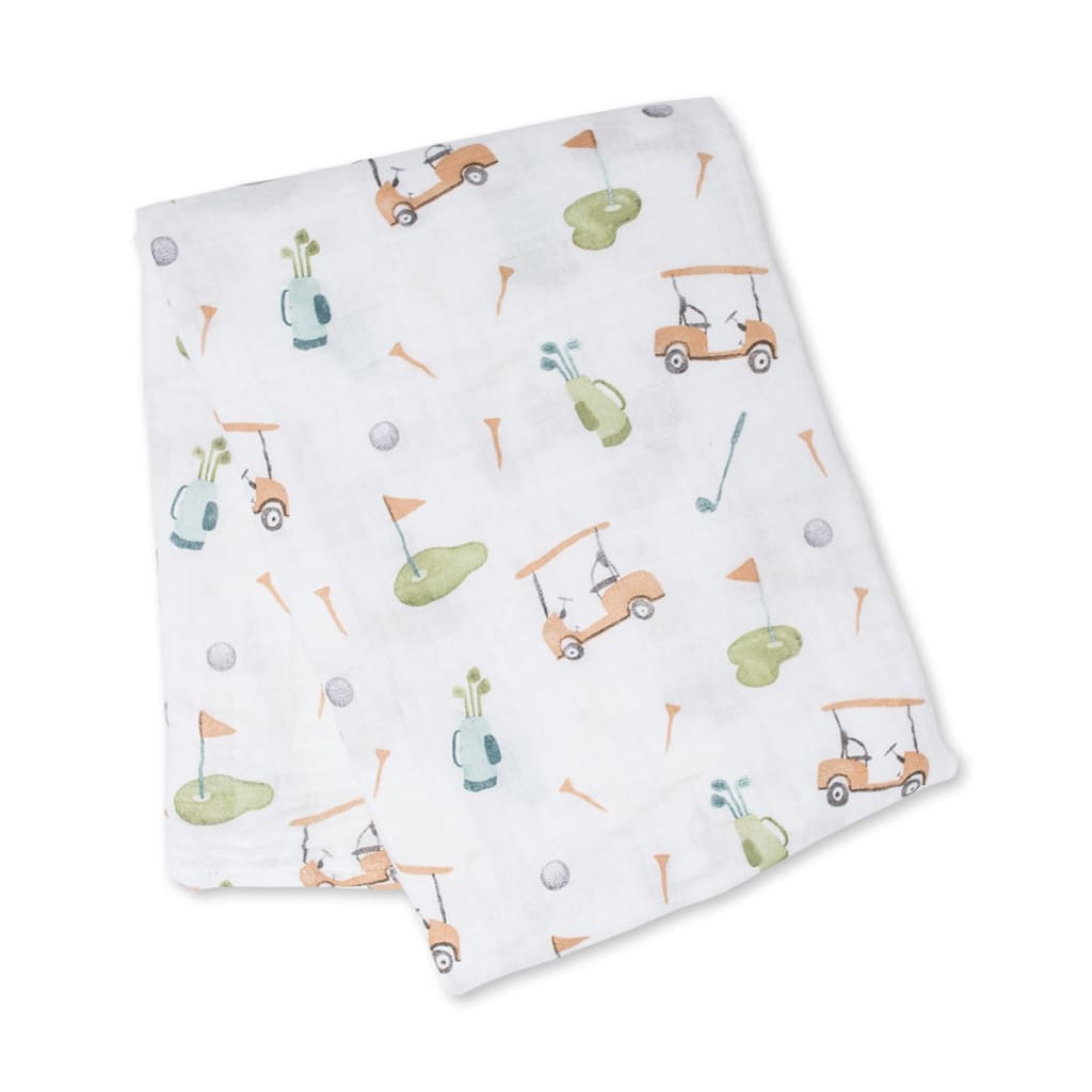 A folded white muslin baby swaddle blanket featuring a playful golf course print with orange golf carts, green putting greens, blue tees, and orange tees.