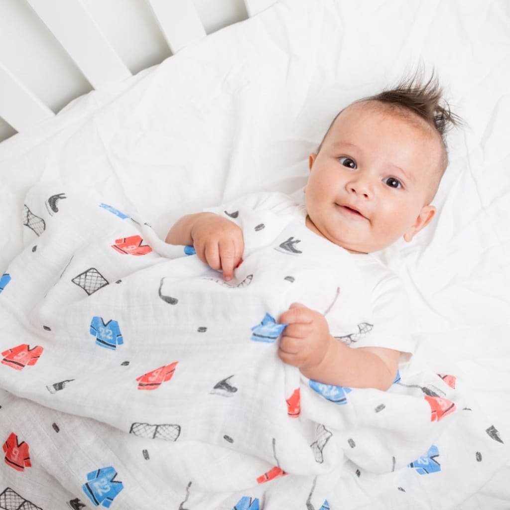 Baby wrapped in a white blanket with colorful patterns, lying on a white surface.