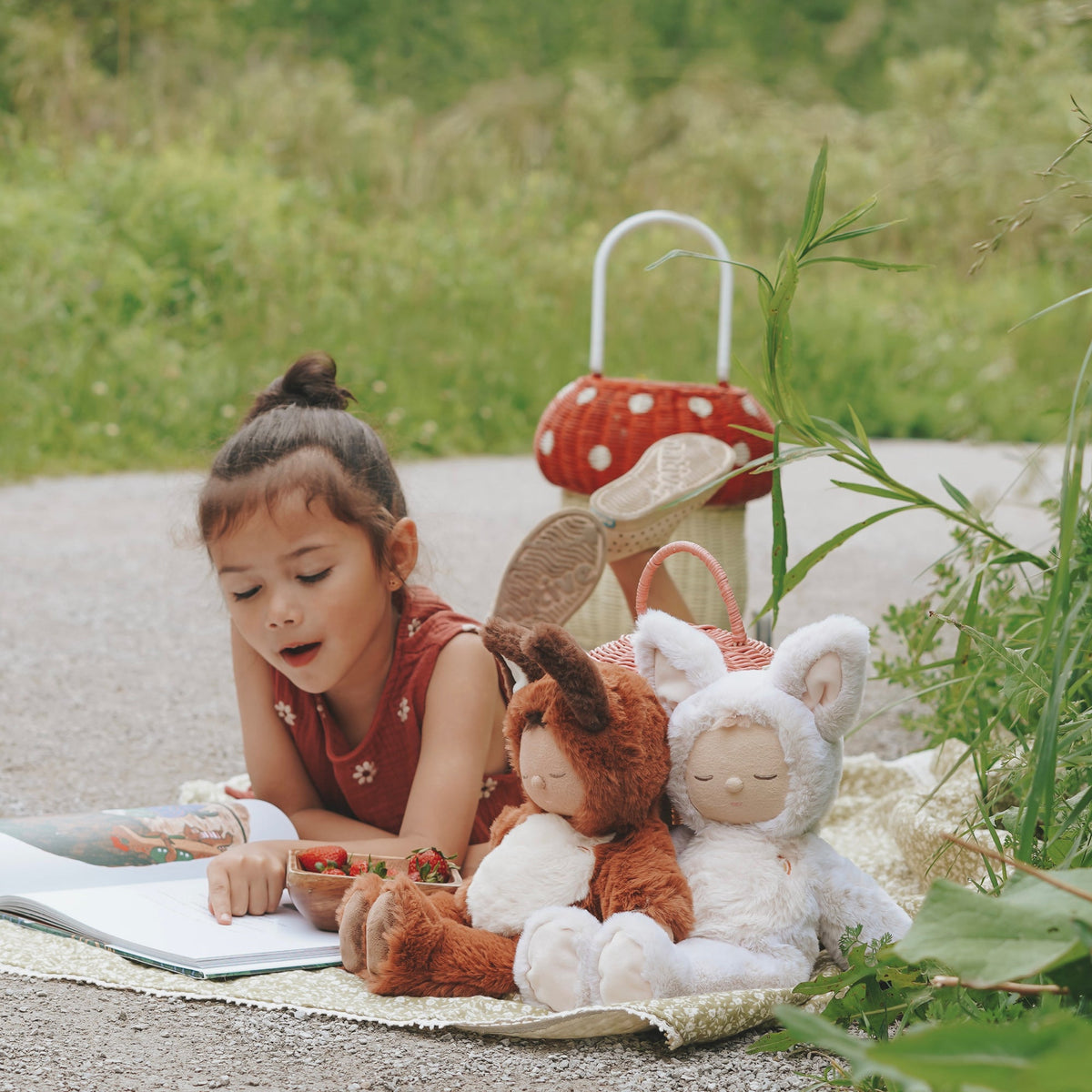 Child reading a book with two plush toys outdoors