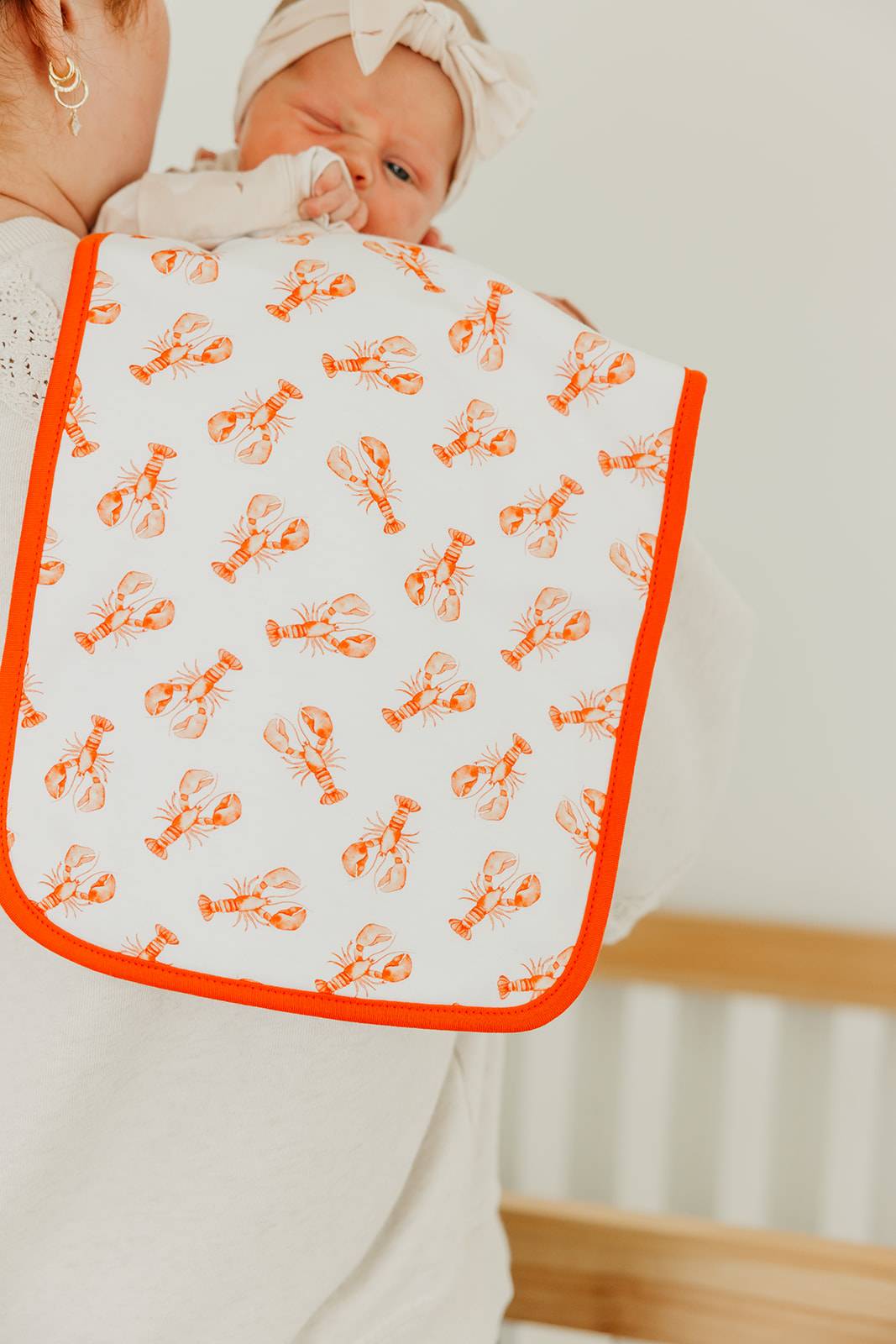 Baby wearing a bib with orange lobster pattern on a white background
