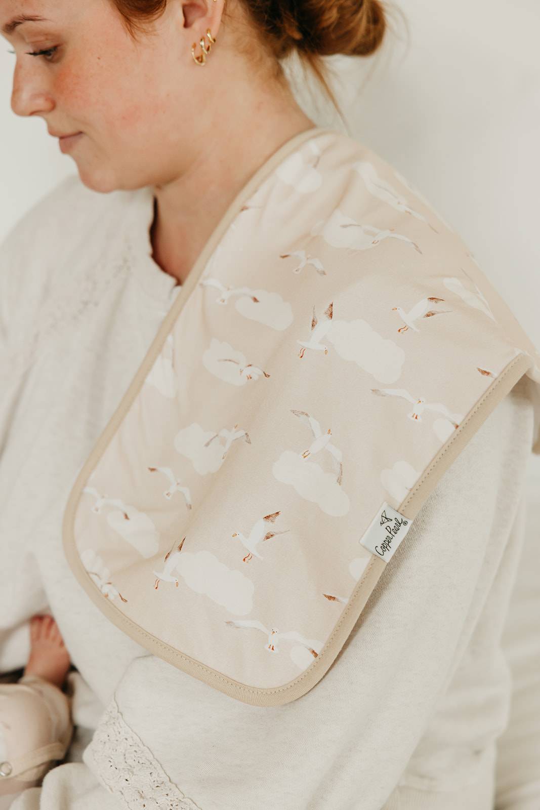 Person wearing a beige bib with a pattern, sitting on a white blanket.