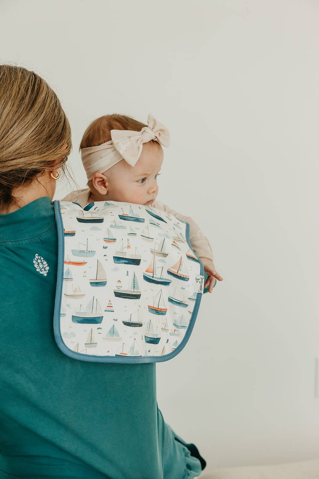 Woman holding a baby wearing a bib with boat pattern against a plain background