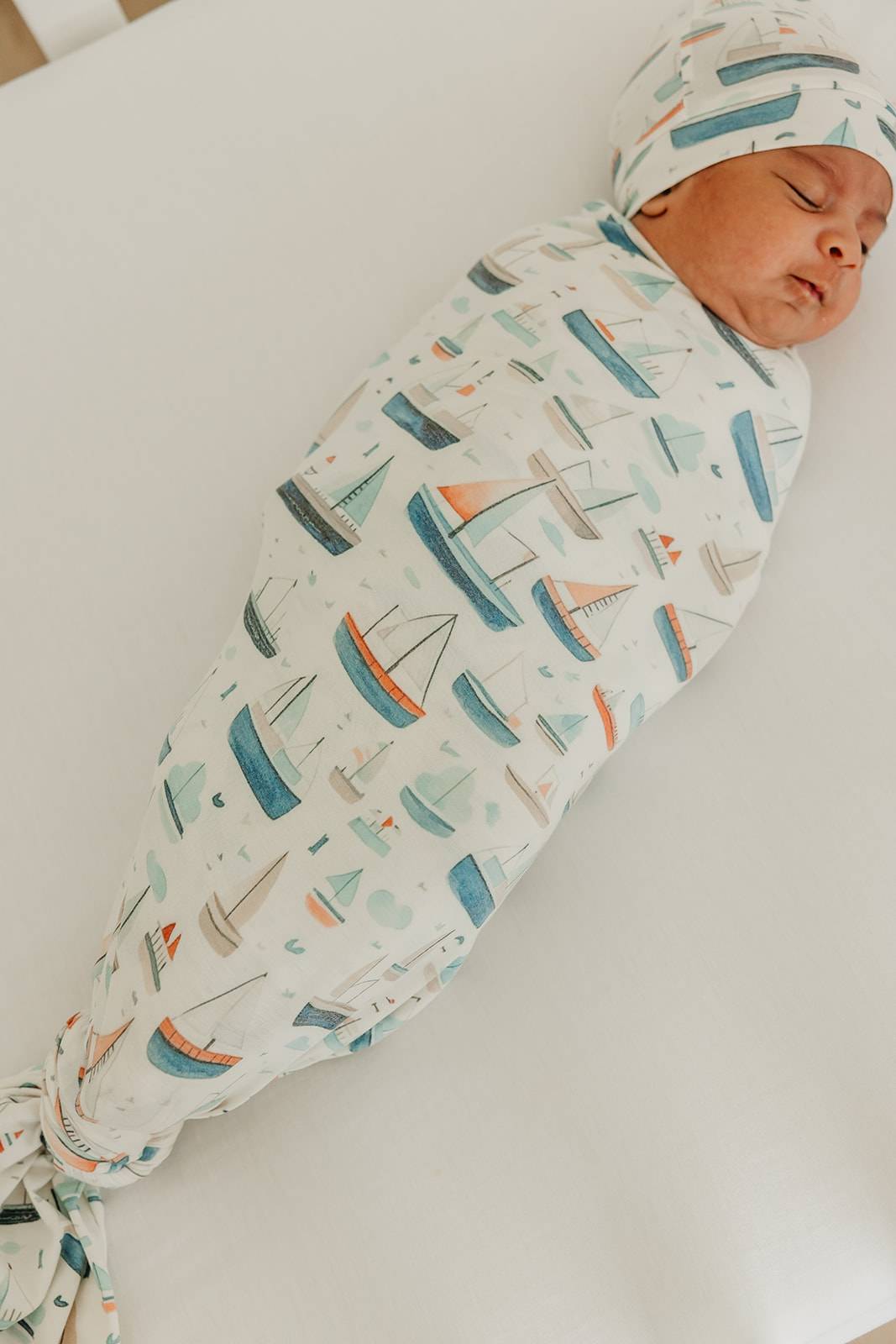 Newborn baby swaddled in a blanket with boat pattern on a white surface