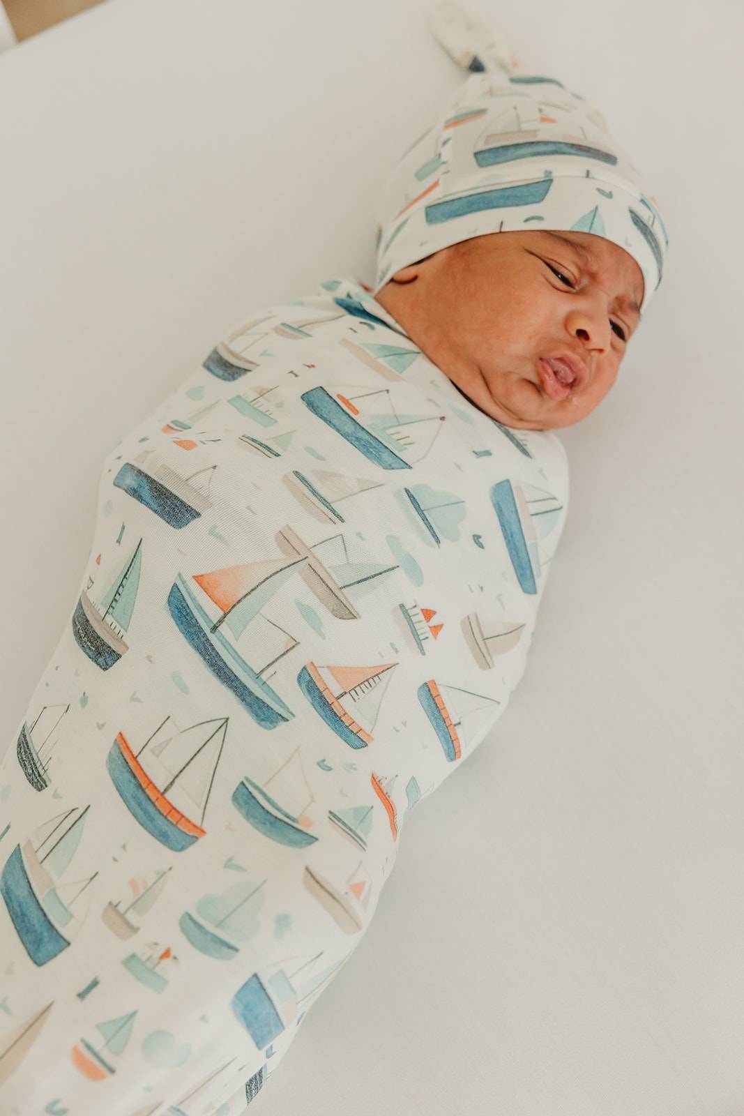 Newborn baby wrapped in a blanket with boat pattern and wearing a matching hat.