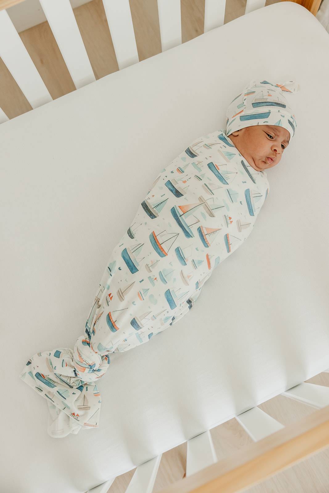 Newborn baby swaddled in a blanket with boat pattern in a crib
