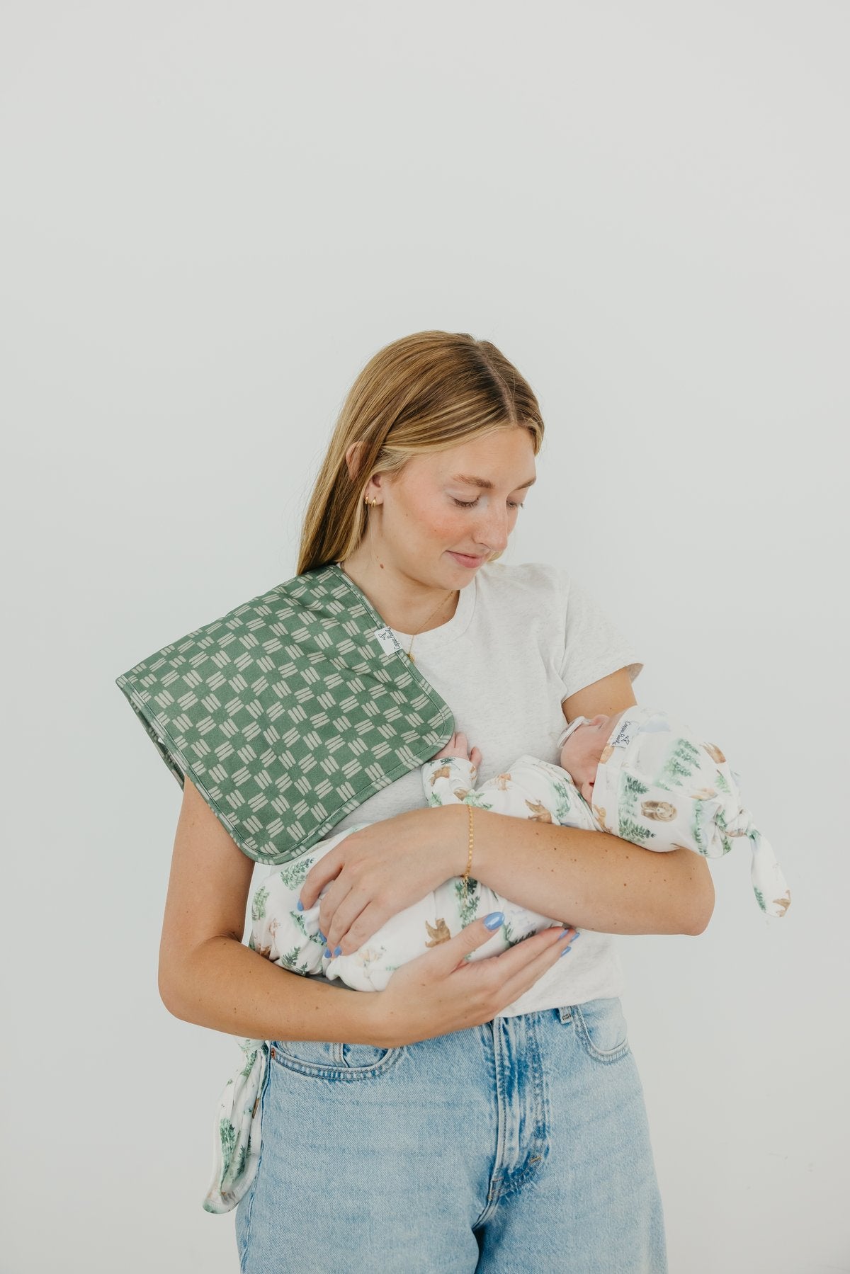 Woman holding a baby wrapped in a green and white checkered blanket against a plain background