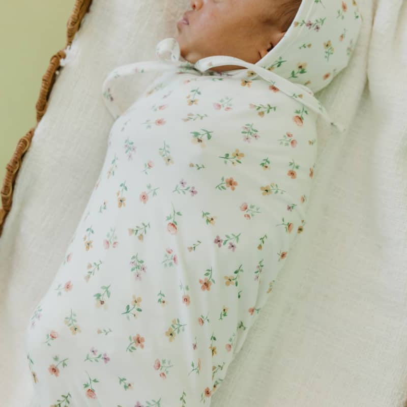 Baby wrapped in a floral swaddle blanket on a soft surface