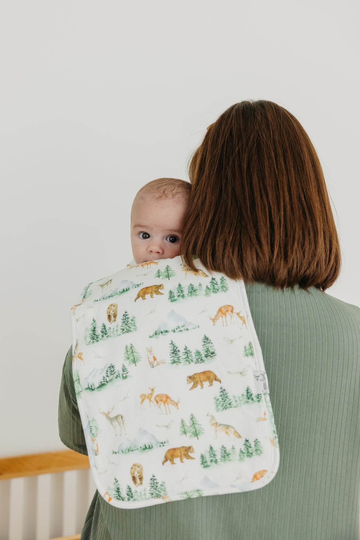 Woman holding a baby with a forest-themed blanket