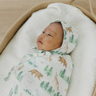 Newborn baby wrapped in a forest-themed swaddle blanket with a hood.