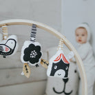 A plush Wee Gallery house stroller toy hanging from an activity gym next to other black-and-white toys, with a baby in the background.