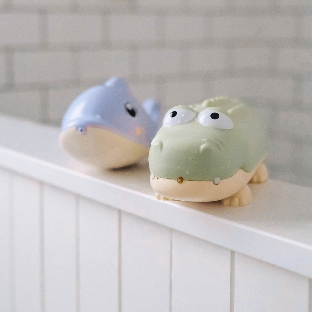Two cartoonish animal figurines, one blue and one green, on a white surface with a tiled wall background.