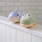 Two cartoonish animal figurines, one blue and one green, on a white surface with a tiled wall background.