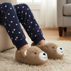 Person wearing navy pajama pants with white stars and brown bear slippers on a carpeted floor.