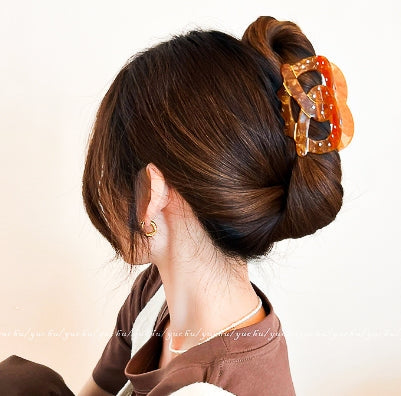 Woman with a stylish hair bun holding an orange hair clip against a neutral background