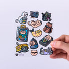 Collection of cat-themed stickers on a white background with a hand holding one sticker.