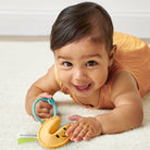 Baby lying on a white blanket with a yellow teething toy