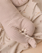 A close-up of a long, cylindrical nursing pillow with thin brown and beige stripes, nestled in a beige patterned blanket with small embroidered deer.