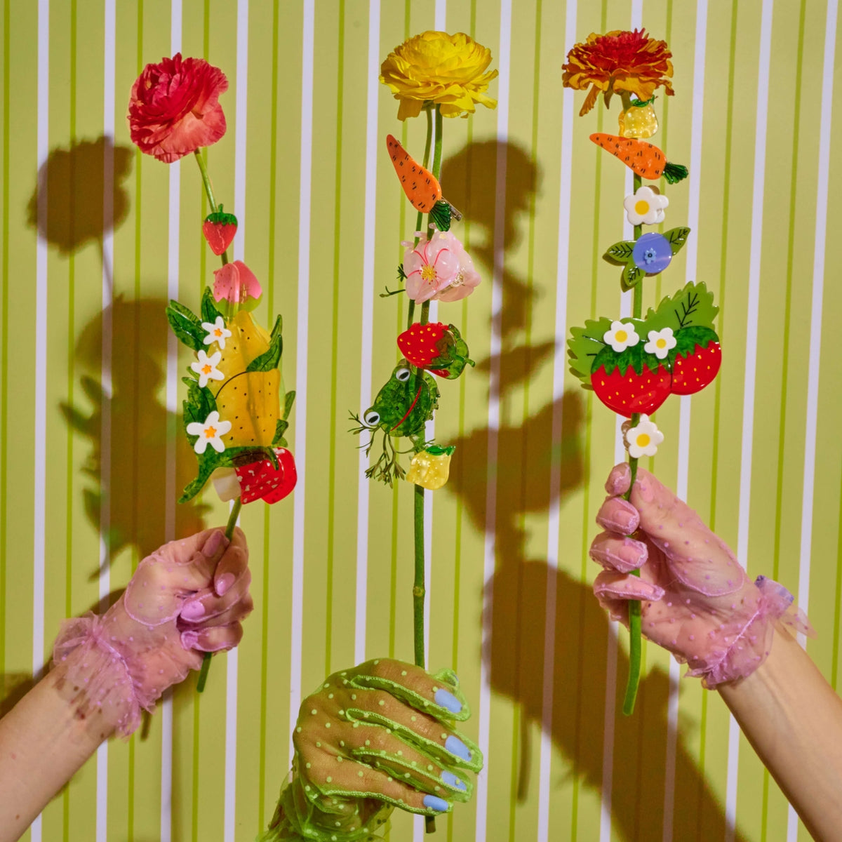 Two hands holding colorful flower sticks against a striped green and white background