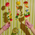 Two hands holding colorful flower sticks against a striped green and white background