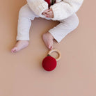 Baby playing with a red crochet rattle on a beige surface