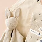 Knitted baby blanket with bunny ears and 'The Blueberry Hill' label on a pink background