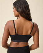 A woman shown from the back wearing a black sports bra and matching black bottoms against a plain beige studio background.