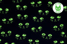 Black fabric with a repeating pattern of glowing neon green cat faces, featuring a circular 'My Eyes Glow' logo in the top right corner.