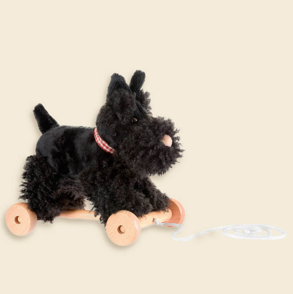 Plush toy dog on wheels with a string on a beige background