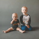 Two young boys wearing 'Little Brother' and 'Big Brother' shirts on a gray background