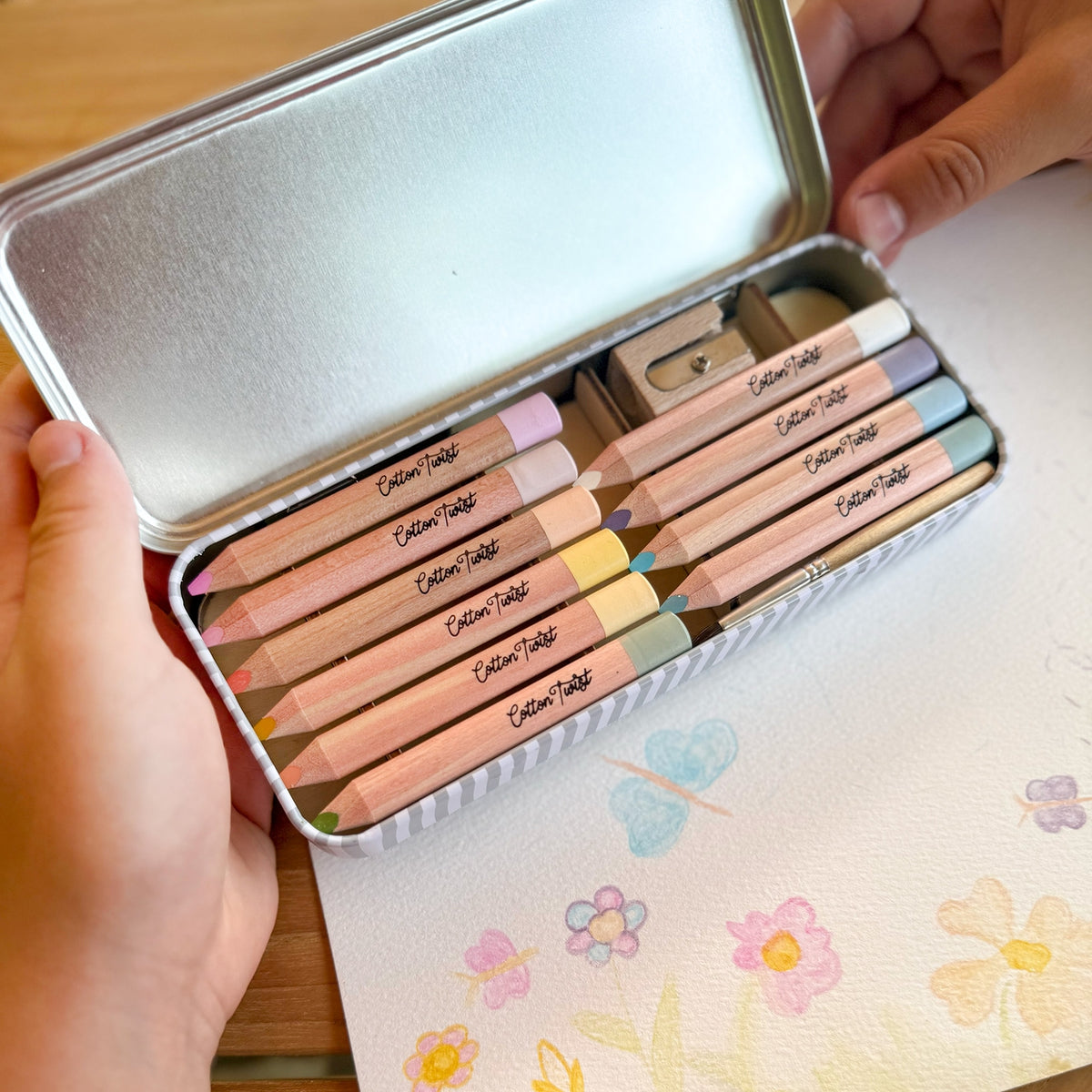Set of colored pencils in a tin with floral design on the paper underneath