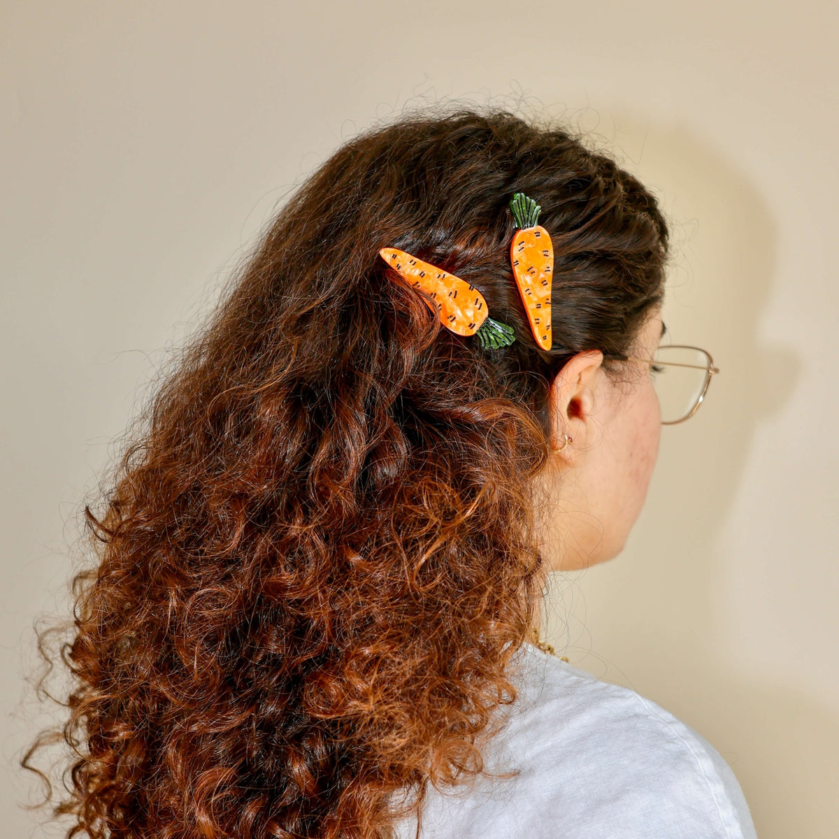 Person with curly hair wearing carrot-shaped hair clips on a plain background