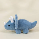 A small blue plush dinosaur toy with white horns and a black eye, photographed on a plain light beige background.