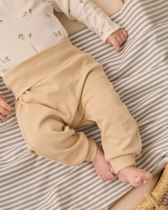 A baby lying on a beige and white striped blanket, wearing beige knit pants and a cream long-sleeve top with small floral prints.
