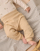 A baby lying on a beige and white striped blanket, wearing beige knit pants and a cream long-sleeve top with small floral prints.