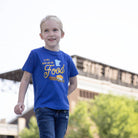 Child wearing a blue t-shirt with 'Here for the Food' text, standing in front of a State Fair sign.