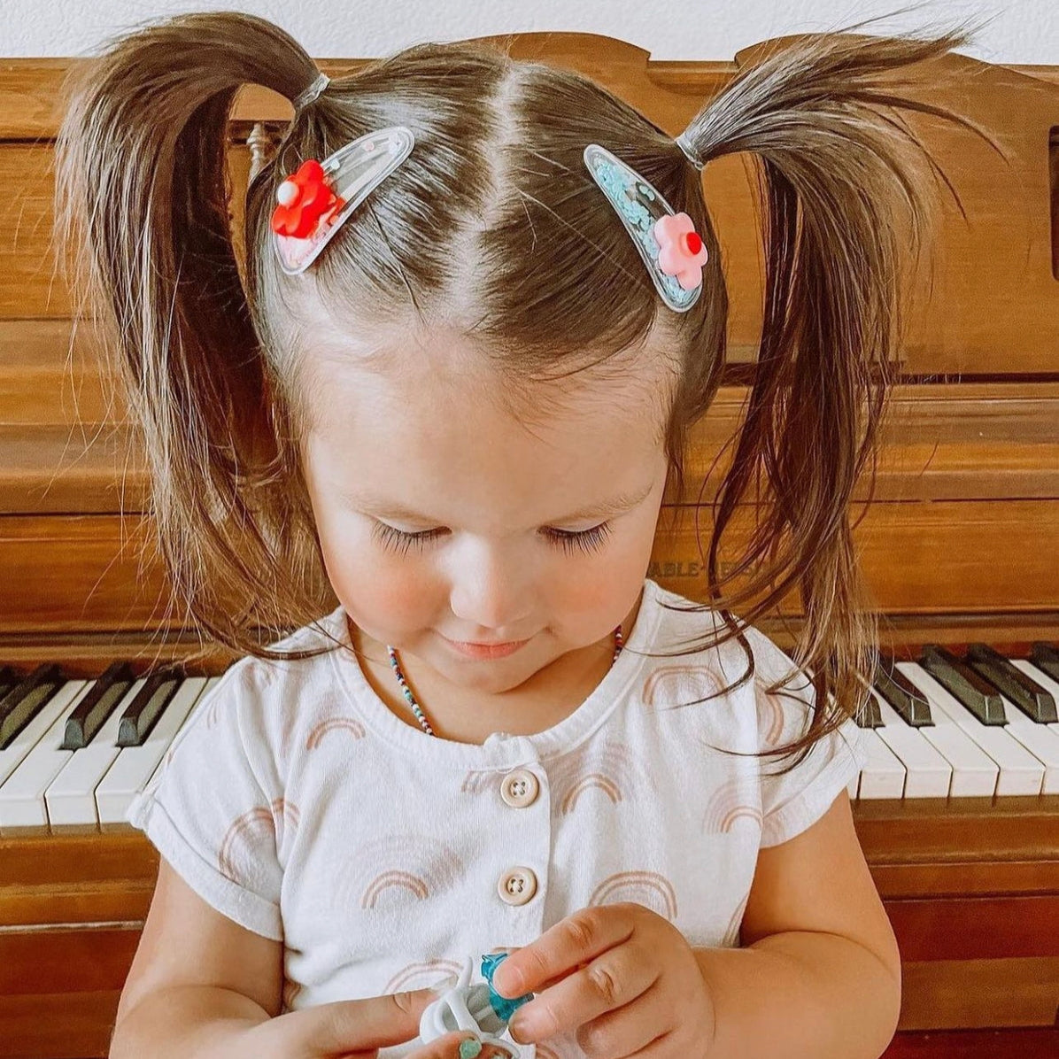 Child with pigtails and hair clips in front of a piano